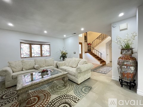 A living room with a glass coffee table and a staircase in the background.