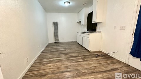 A room with wooden flooring and white walls, featuring a small kitchenette with a refrigerator, microwave, and oven.