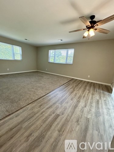 A room with a ceiling fan and light, carpeted floor, and two windows.