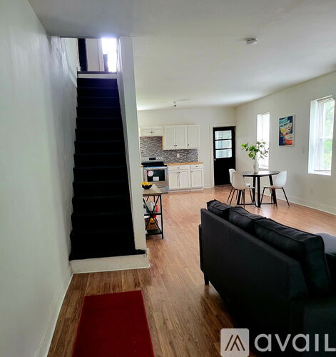 A living room with a black couch and a red rug.