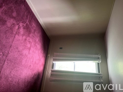 A room with a window and a wall with a purple wallpaper.