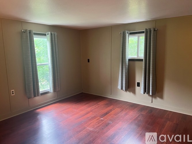 A room with wooden floors and two windows with curtains.