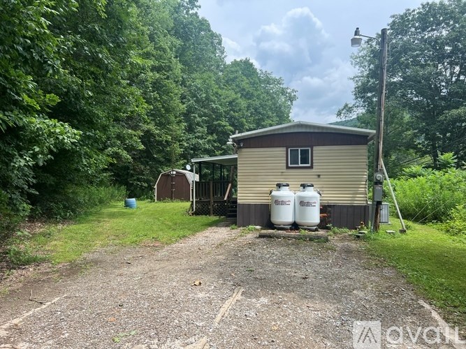 A green barrel sits on a grassy field next to a wooden shed.