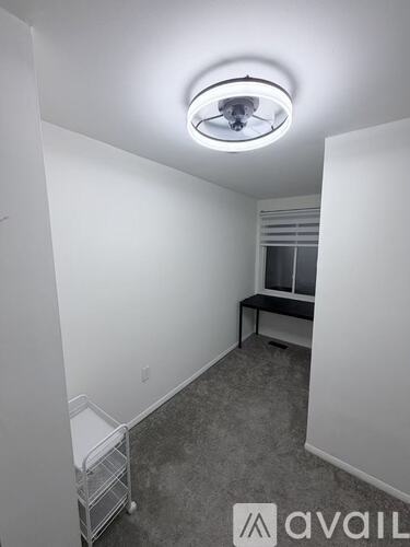 A white chair is placed in a corner with a black desk and a window.