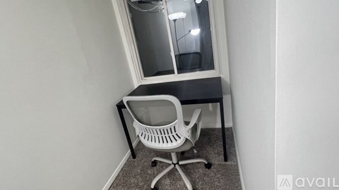 A white chair is placed in a corner with a black desk and a window.