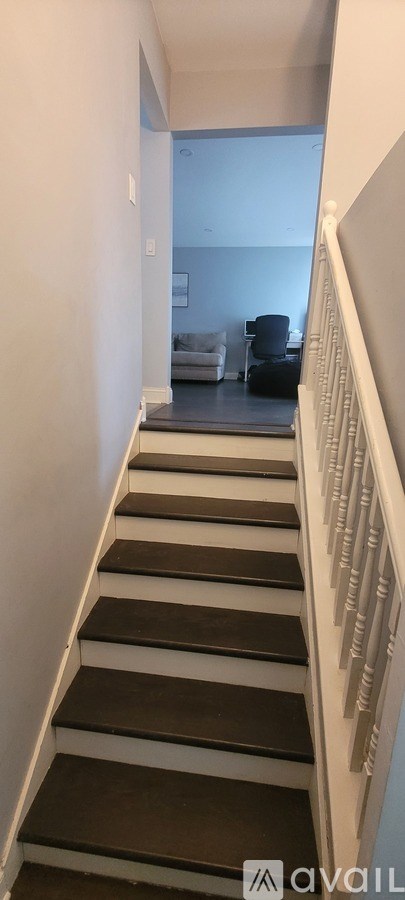 A staircase with a white railing and black steps leading to a living room.