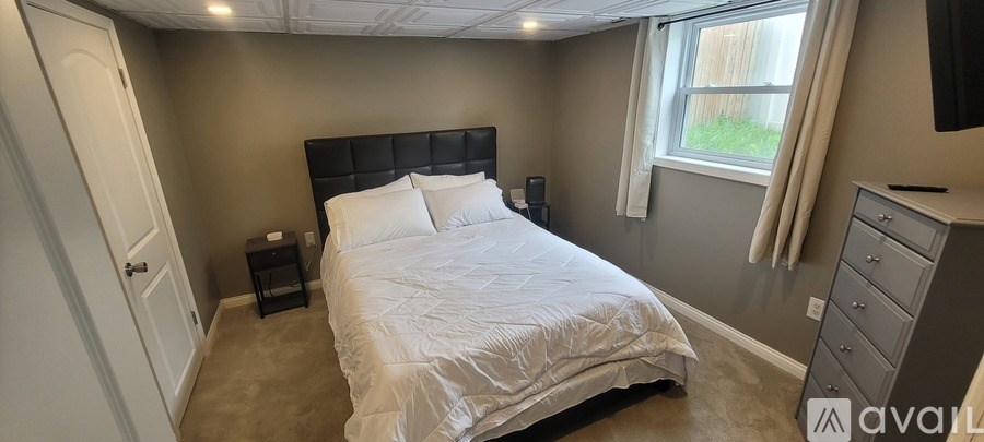 A bedroom with a large bed and a window with white curtains.