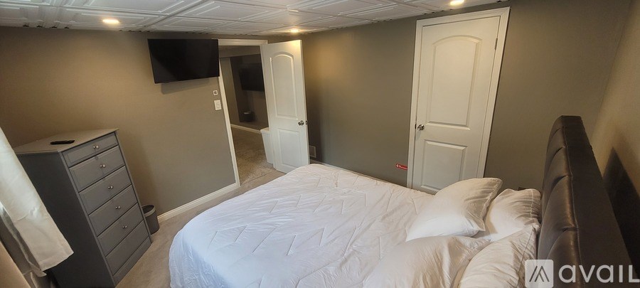 A bedroom with a bed, dresser, and a television on the wall.