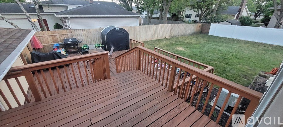 A wooden deck with a railing and a white fence in the background.