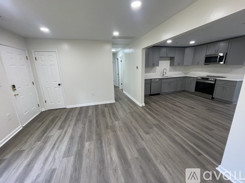 A spacious kitchen and living room with grey flooring and white walls.