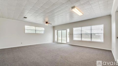 A spacious room with a carpeted floor, ceiling fan, and large windows.