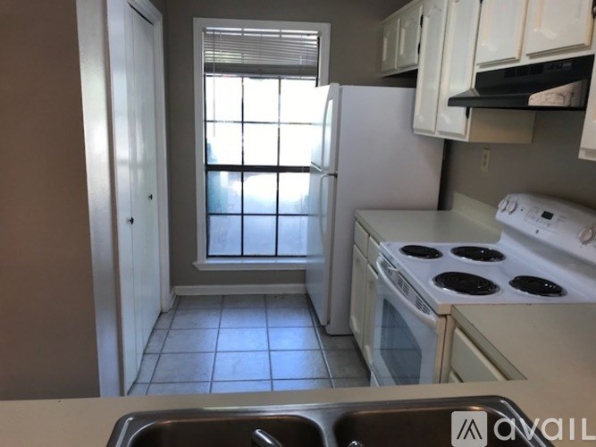 A kitchen with white appliances and a window with blinds.