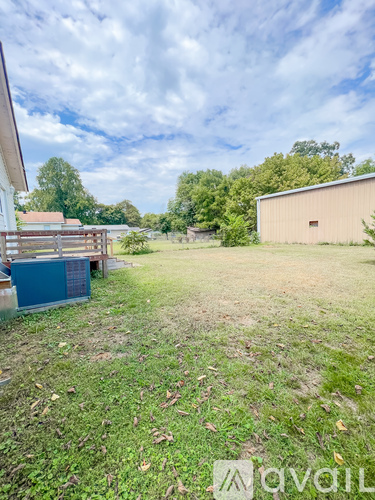 A grassy field with a building and trees in the distance.