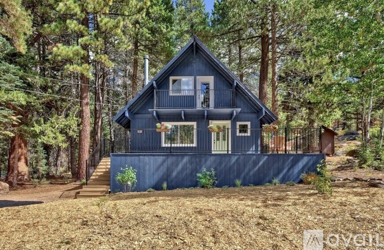 A blue house with a porch and a balcony is surrounded by trees.