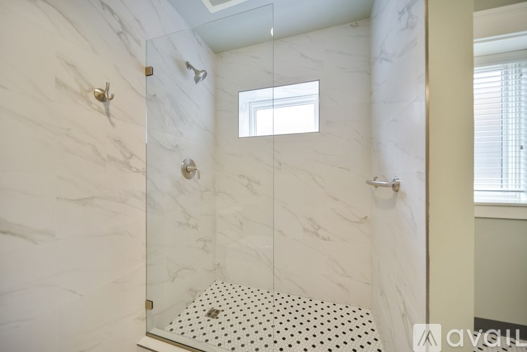 A white marble bathroom with a shower and a window.
