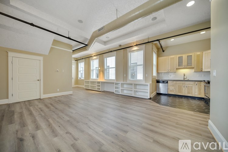 A spacious room with wooden flooring and a kitchen area with cabinets and a dishwasher.