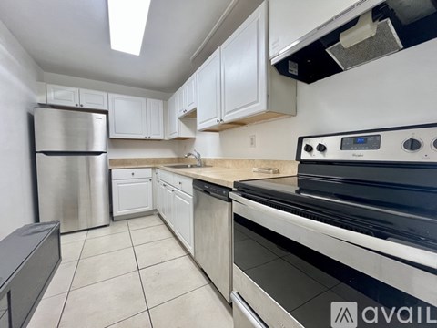 A kitchen with a stainless steel refrigerator, white cabinets, and a black stove top oven.