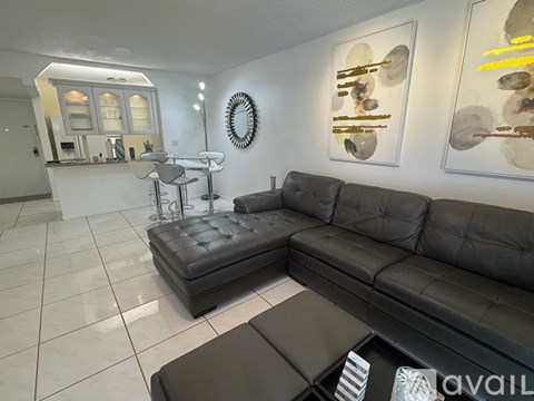 A black leather sofa sits in a well-lit living room with a bar area in the background.