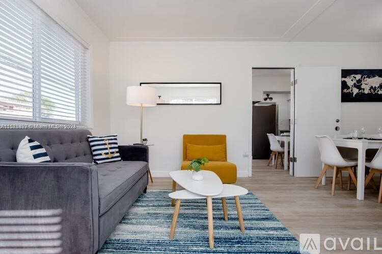 A grey couch with blue and white striped pillows sits in a room with a yellow chair and a white table.