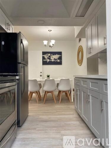 A kitchen with a black fridge and a white chair.