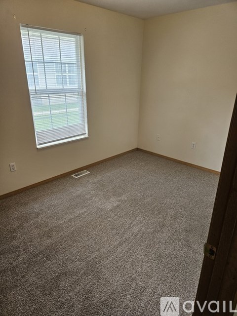 A carpeted room with a window and a door.