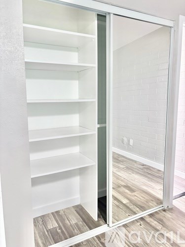 A white shelving unit with a mirrored door is open, revealing a white brick wall and wooden flooring.
