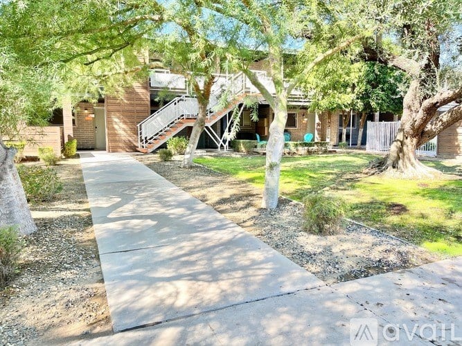 A concrete pathway leads to a house with a tree in front.