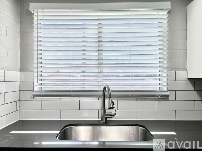 A modern kitchen with a stainless steel sink and white tiled walls.