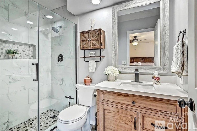 A bathroom with a white toilet, a marble shower, and a wooden vanity.
