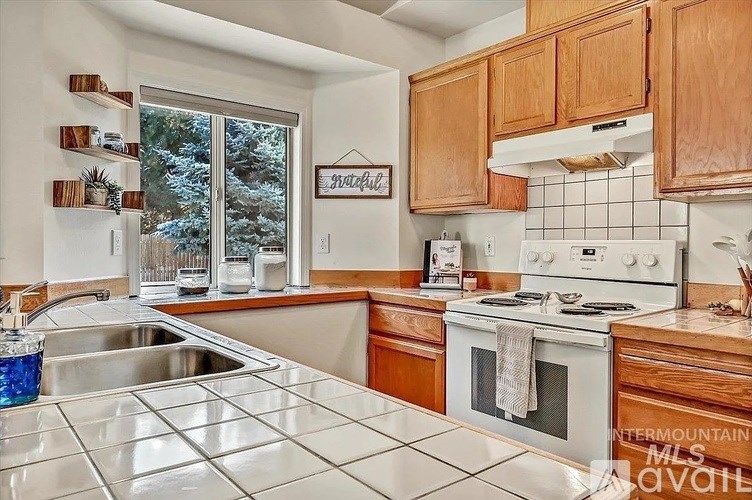A kitchen with a stove, sink, and wooden cabinets.
