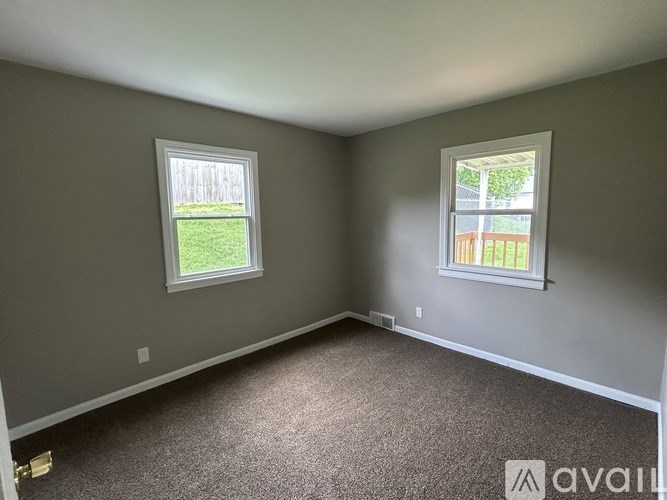 A room with two windows, one facing a green lawn and the other a wooden fence.
