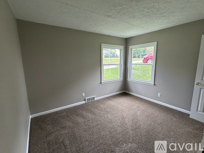 A room with carpeted floor and two windows.