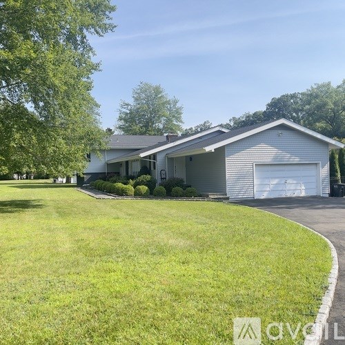 A house with a grey roof and a white garage door is surrounded by a green lawn.