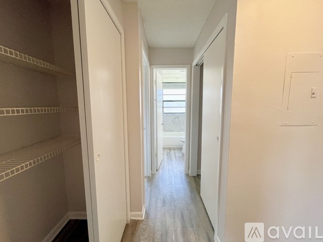 A room with wooden floors and white walls, leading to a kitchen area.