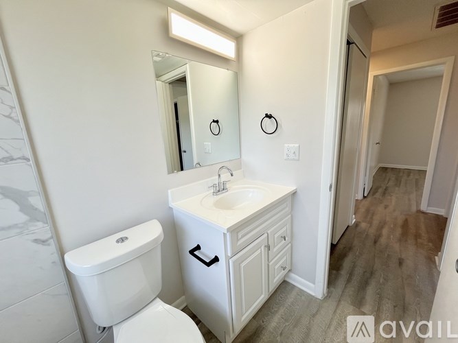 A room with wooden floors and a kitchen area in the background.