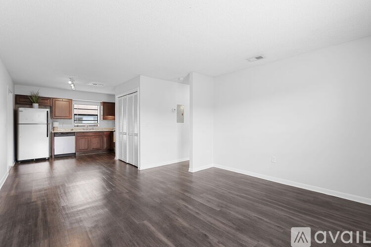 A spacious room with wooden flooring and a kitchen area in the background.