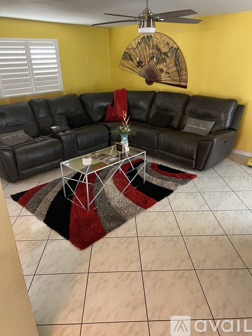 A living room with a black leather couch and a fan on the ceiling.