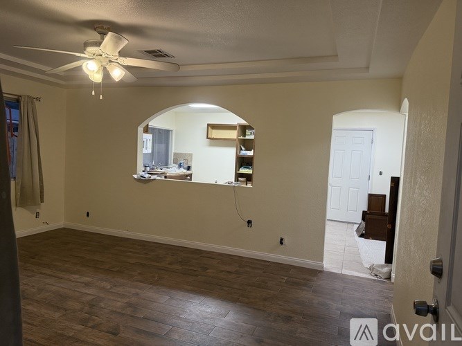 A room with a ceiling fan and a window with a view of a kitchen.