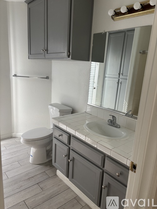 A bathroom with a toilet, sink, and cabinets.