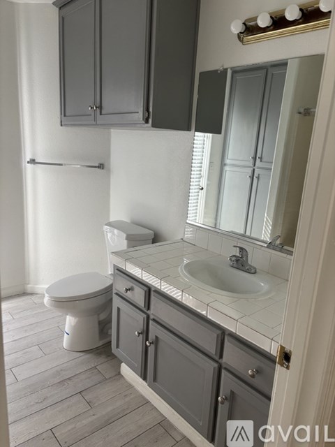 A bathroom with a toilet, sink, and cabinets.