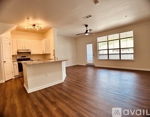 A spacious living room with hardwood floors and a kitchen area in the background.