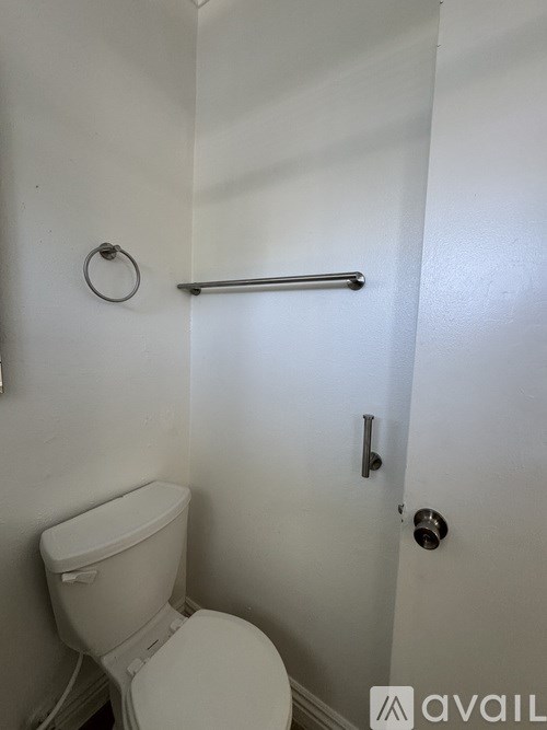 A white toilet in a small bathroom with a towel bar on the wall.