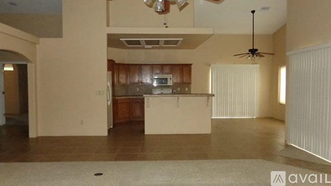 A spacious living room with a kitchen in the background and a fan on the ceiling.