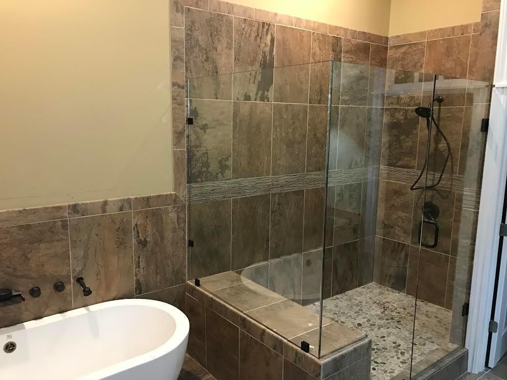 A bathroom with a tiled shower and a white bathtub.