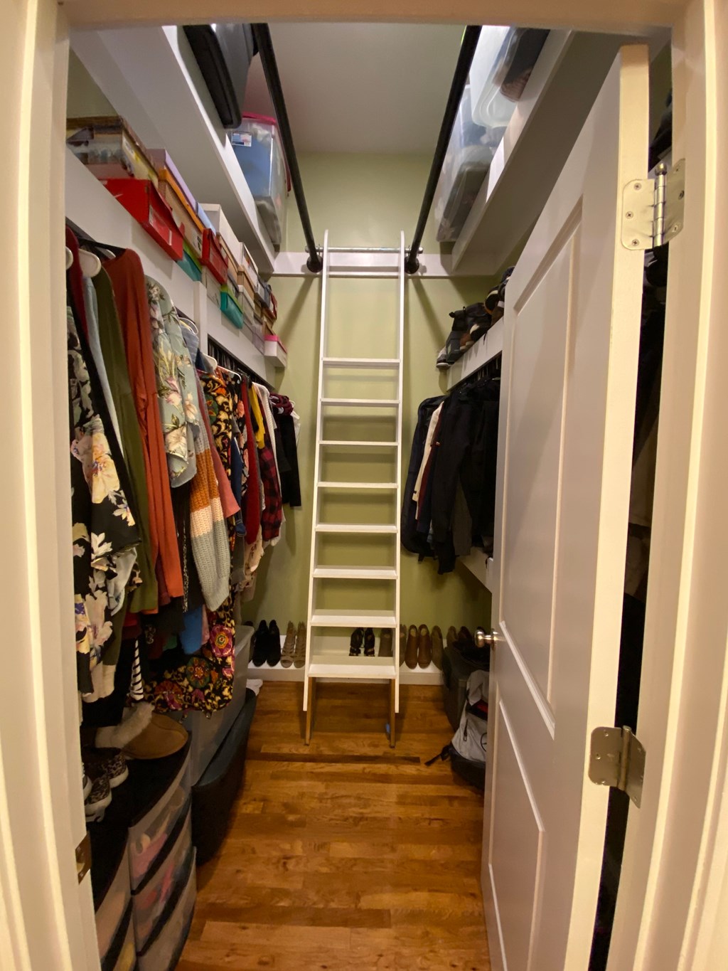 A walk in closet with a white door and a white shelf.