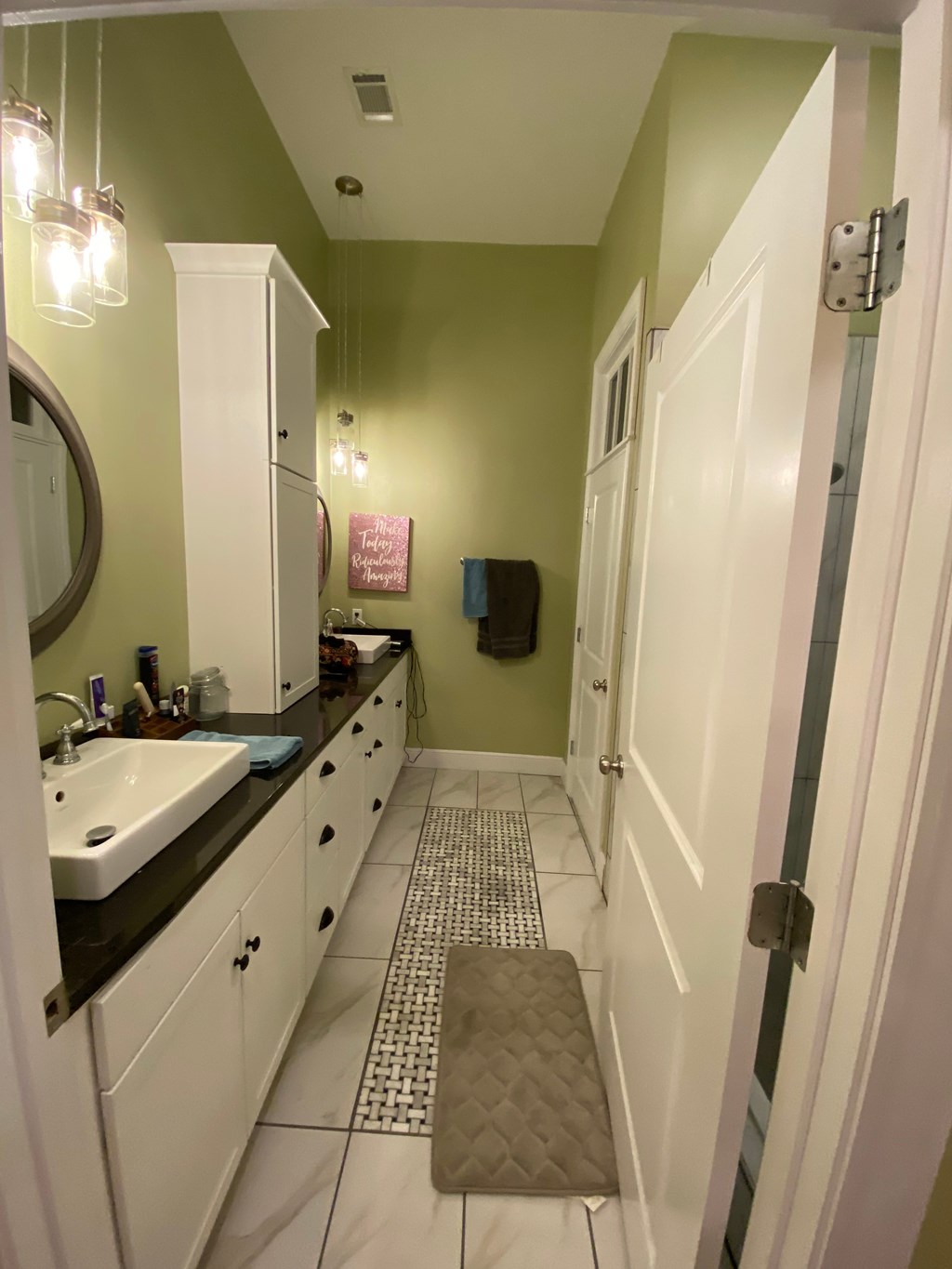 A bathroom with green walls and white cabinets.