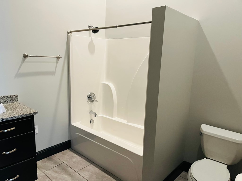 A white bathtub with a shower head and a white toilet in a bathroom.