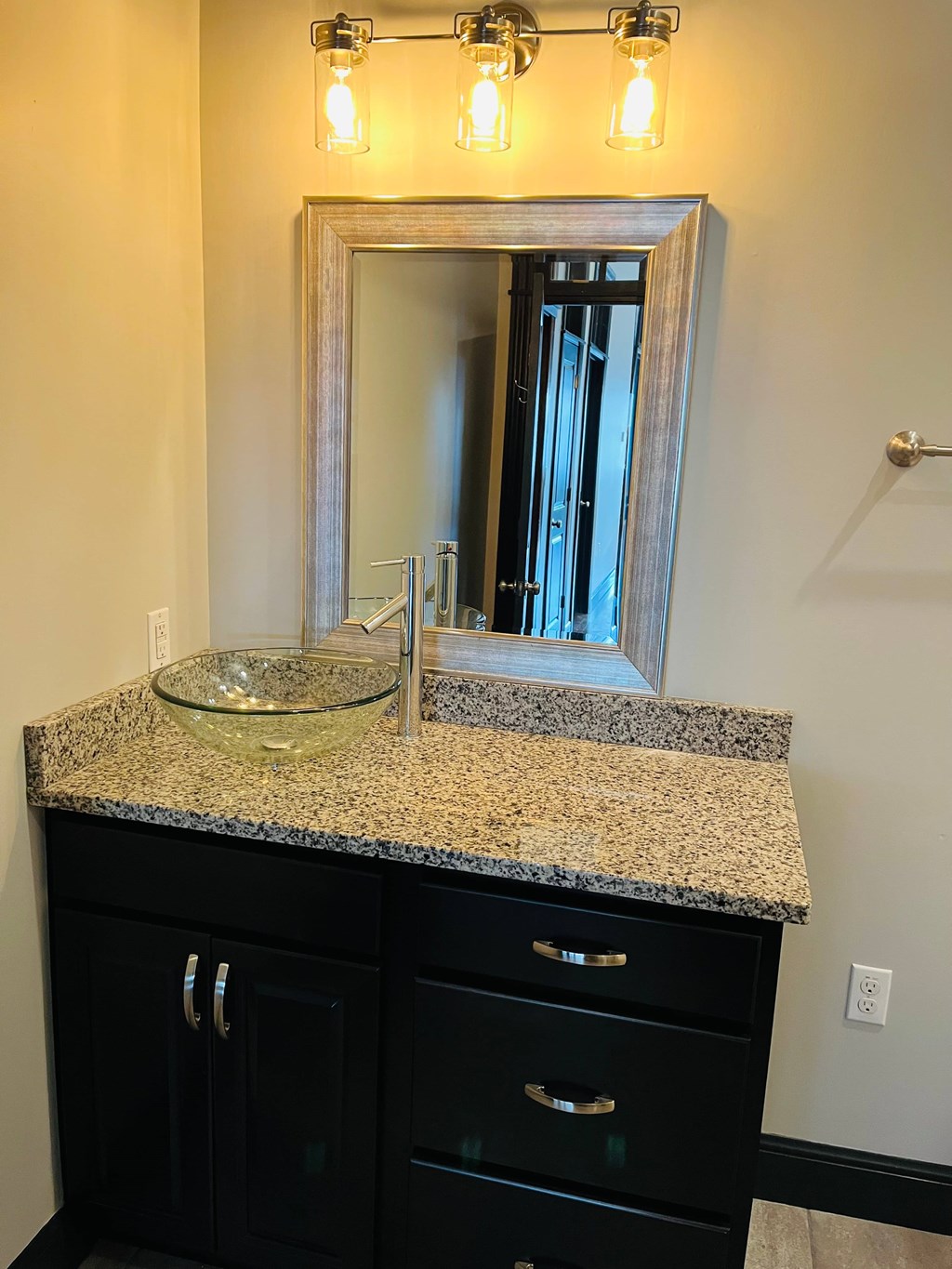 A bathroom vanity with a granite countertop and a mirror above it.