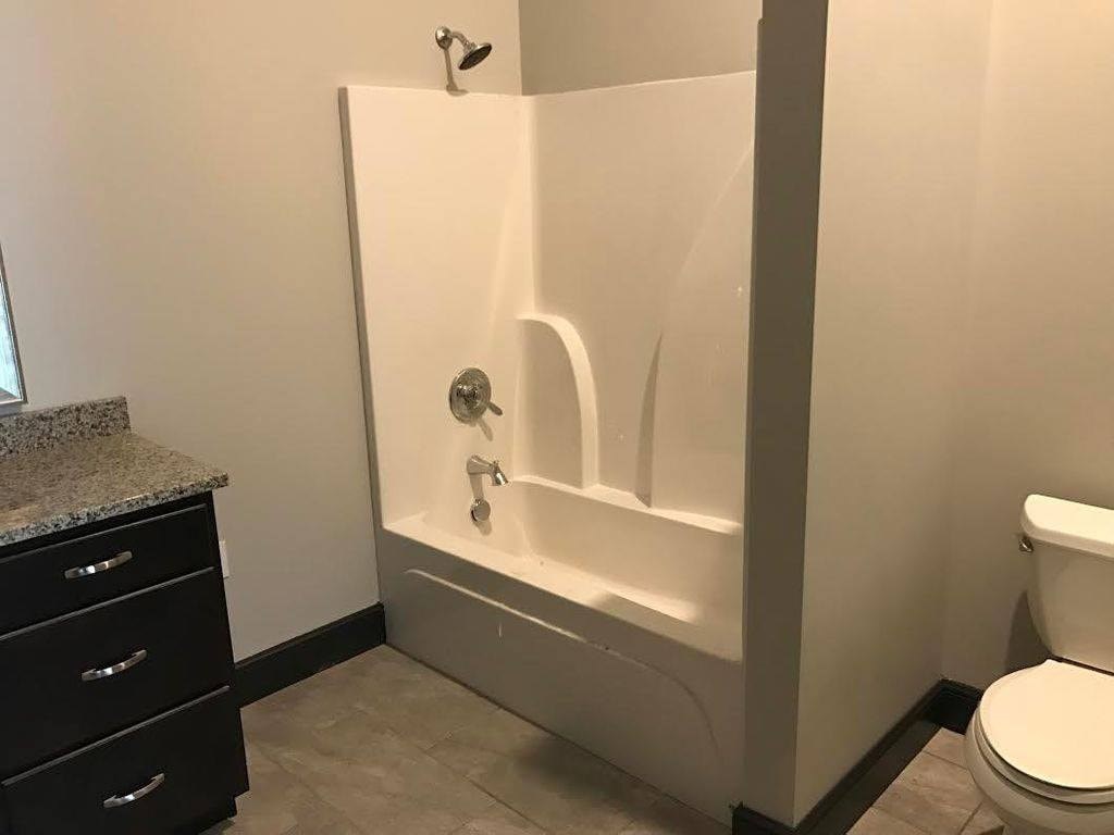 A white bathtub with a shower head and a toilet in a bathroom.