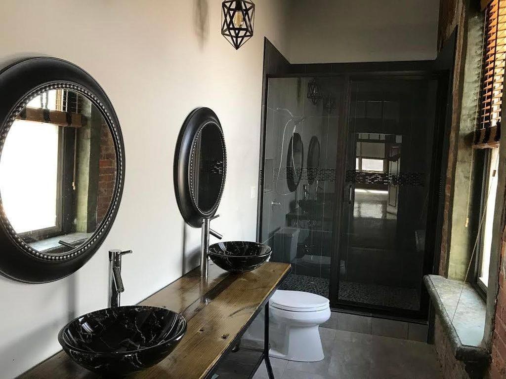 A bathroom with a toilet, sink, mirrors and a shower.